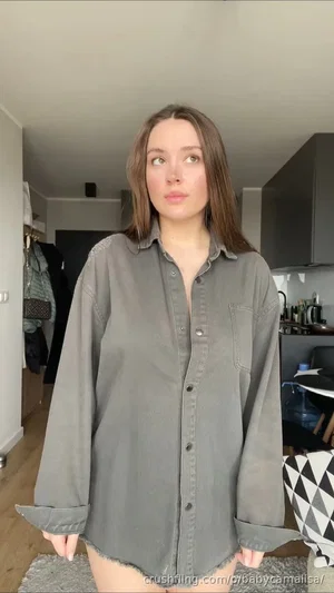 Woman in oversized gray shirt, standing indoors, legs bare, casual home setting.