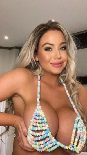 Woman with blonde hair wearing colorful beaded top, posing indoors.