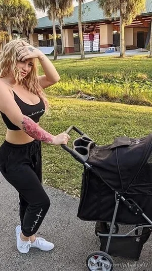 Woman with blonde hair in black crop top and pants, pushing stroller outdoors.