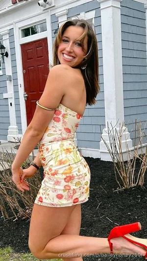Woman in floral strapless dress posing outdoors in front of house.