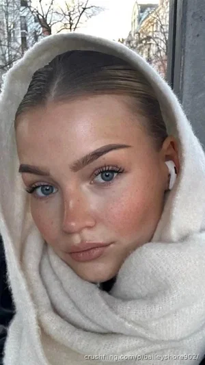 Woman with blue eyes and freckles wearing white hooded scarf, outdoor setting.