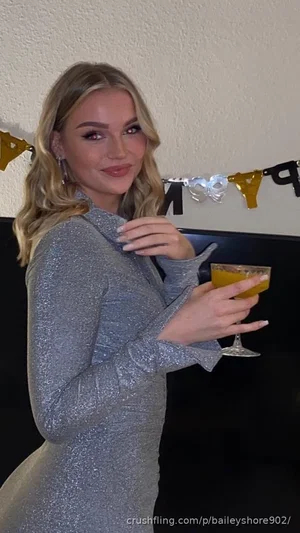 Woman in a silver sparkly dress holding a drink, standing indoors near a wall with party