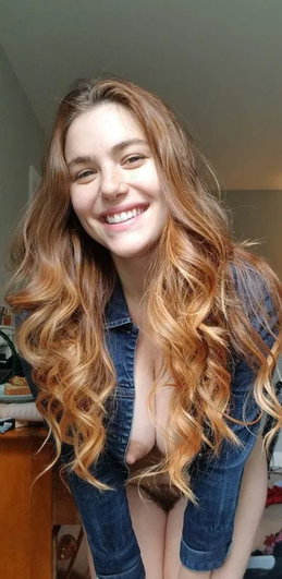 Smiling woman with long wavy hair in open denim jacket.
