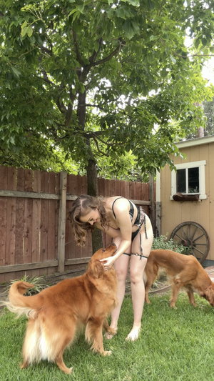 Curvy woman in black lingerie with dogs in backyard.