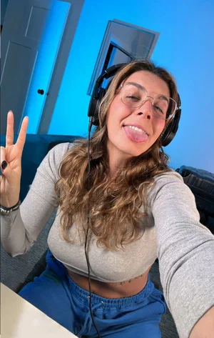 Woman with brown hair, glasses and headphones in grey top indoors.