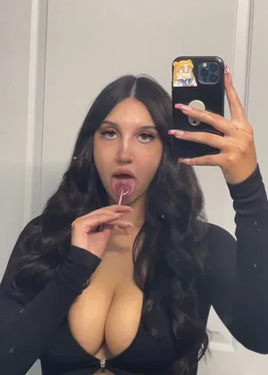 Woman with long dark hair taking mirror selfie in black top indoors.