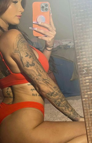 Woman with tattoos posing in red lingerie for a mirror selfie.
