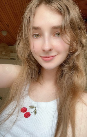 Blonde woman with long hair in white tank top taking selfie indoors.