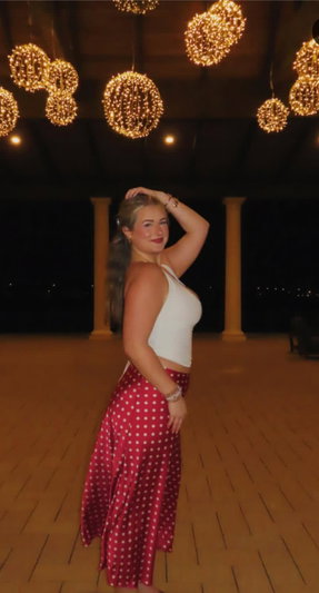 Woman in white top and red polka dot skirt posing at night.