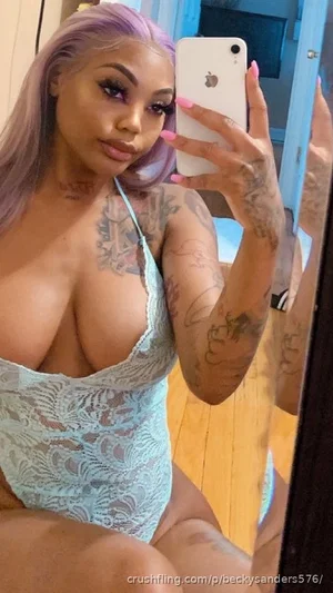 Woman with purple hair and tattoos wears light blue lace bodysuit, taking mirror selfie indoors.