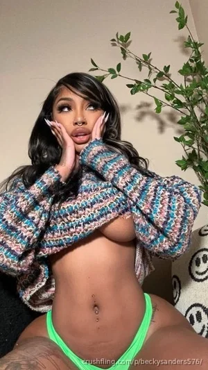 Woman with long dark hair in a colorful sweater and green thong, posing indoors with hands on face.