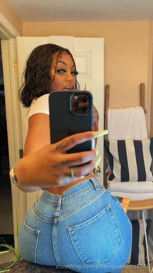 Woman with curly hair in white crop top and jeans, taking mirror selfie indoors.