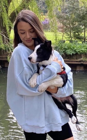 Slim woman in blue hoodie and black shorts holds puppy outdoors.
