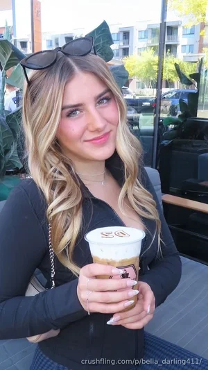 Woman with blonde hair in black top holding coffee cup outdoors.