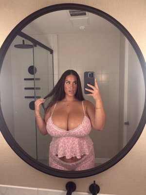 Woman in pink lace lingerie taking mirror selfie in bathroom.