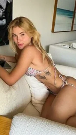 Blonde woman in floral bikini posing on white couch indoors.