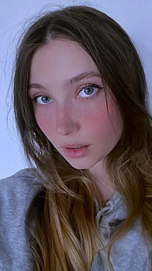 Woman with long brown hair and blue eyes wearing a gray hoodie, indoors.