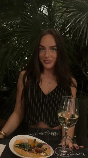 Woman with long dark hair in a striped top sits at a table with food and wine, surrounded by green