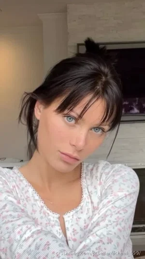 Woman with dark hair and blue eyes wearing floral top indoors.