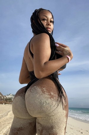 Curvy woman with braids in black bikini on beach.