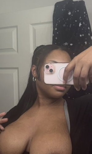 Curvy black woman in low-cut top takes indoor selfie.