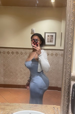 Curvy black woman in blue dress, bathroom mirror selfie.