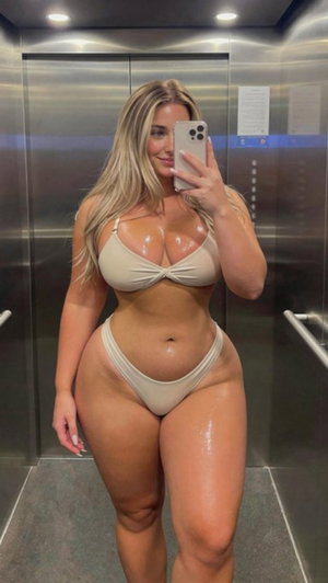 Woman with blonde hair in beige bikini taking mirror selfie in elevator.