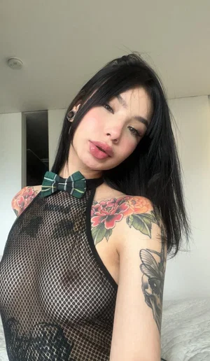 Tattooed woman with long black hair in sheer top and bow tie.