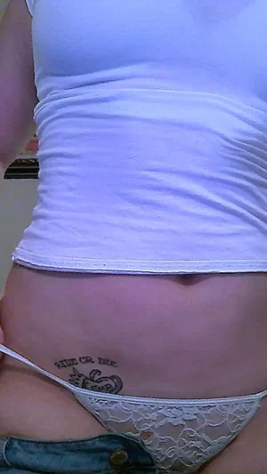 Woman in white crop top and lace underwear, showing tattoo on lower abdomen.
