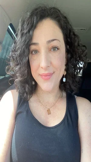 Woman with curly dark hair wearing black tank top, sitting in car.