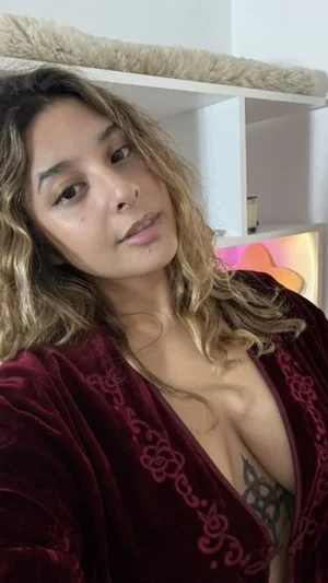 Woman with wavy hair in a red velvet robe, showing chest tattoo, indoor setting.