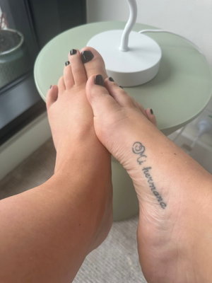 Crossed feet with black nail polish and ankle tattoo indoors.