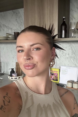 Woman with tattoos and piercings taking selfie in kitchen.