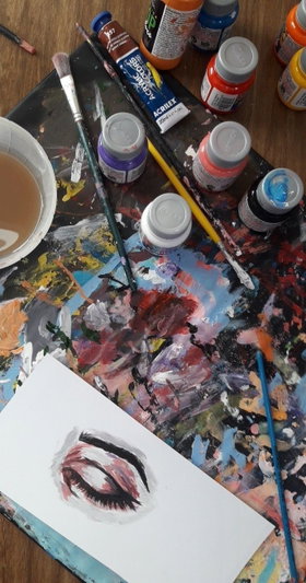 Paintbrushes, paint tubes, and a palette with colorful paint splatters on a wooden table.