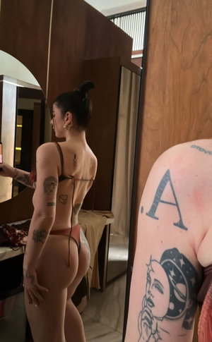 Woman with tattoos in lingerie taking mirror selfie in indoor setting.