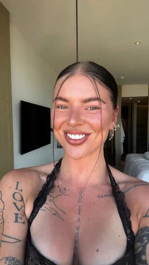 Woman with tattoos wearing black lace top, smiling indoors.