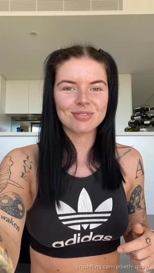 Woman with tattoos wearing black Adidas crop top, indoors in kitchen.
