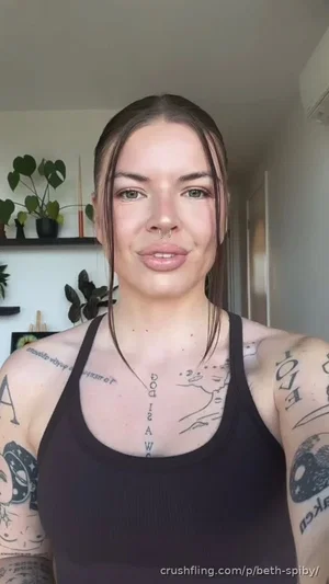 Woman with tattoos wearing black tank top, indoor setting with plants.