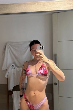 Woman with tattoos in floral bikini taking mirror selfie indoors.