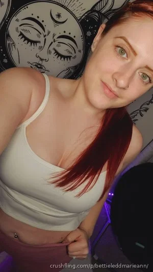 Woman with red hair in white tank top, indoor setting with moon-themed pillow.