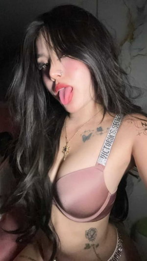 Woman with long dark hair wearing pink bra and tattoos indoors.