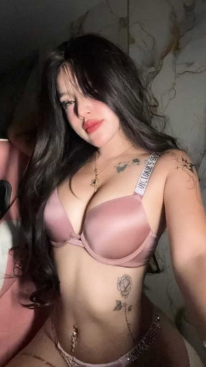 Woman with long dark hair in pink lingerie taking selfie indoors.