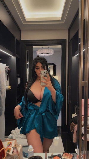 Woman in black bra and blue robe taking mirror selfie in bedroom.
