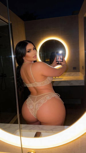 Woman in beige lace lingerie taking mirror selfie in bathroom.