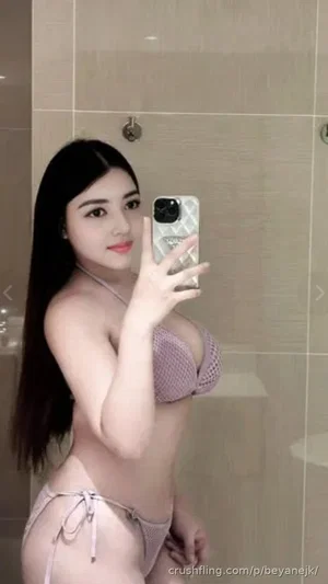 Woman with long dark hair in light purple lingerie taking mirror selfie in tiled bathroom.