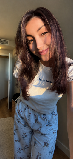 Woman with long dark hair wearing white t-shirt and patterned pants indoors.