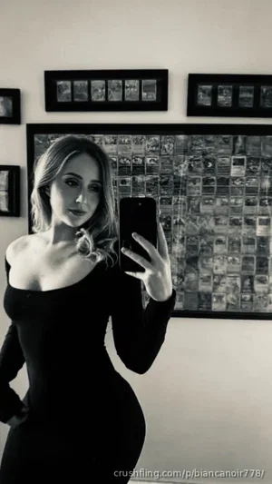 Woman in black off-shoulder dress taking mirror selfie in bedroom.