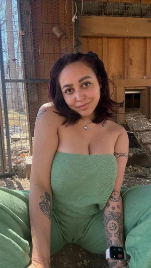 Woman with tattoos in green tube top sitting outdoors near wooden structure.