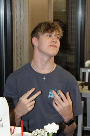 Young man in gray t-shirt making peace signs indoors.