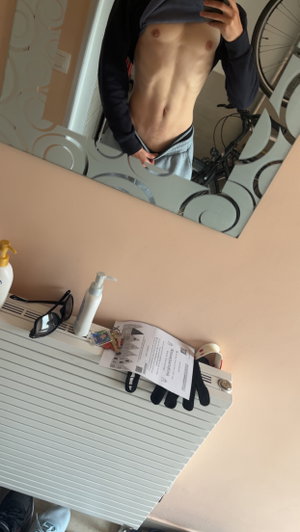 Fit man lifting shirt for mirror selfie indoors.